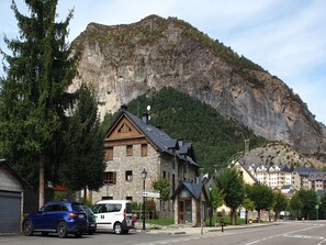 Un edificio de piedra con fachada de madera, un telón de fondo montañoso y una calle con coches aparcados.