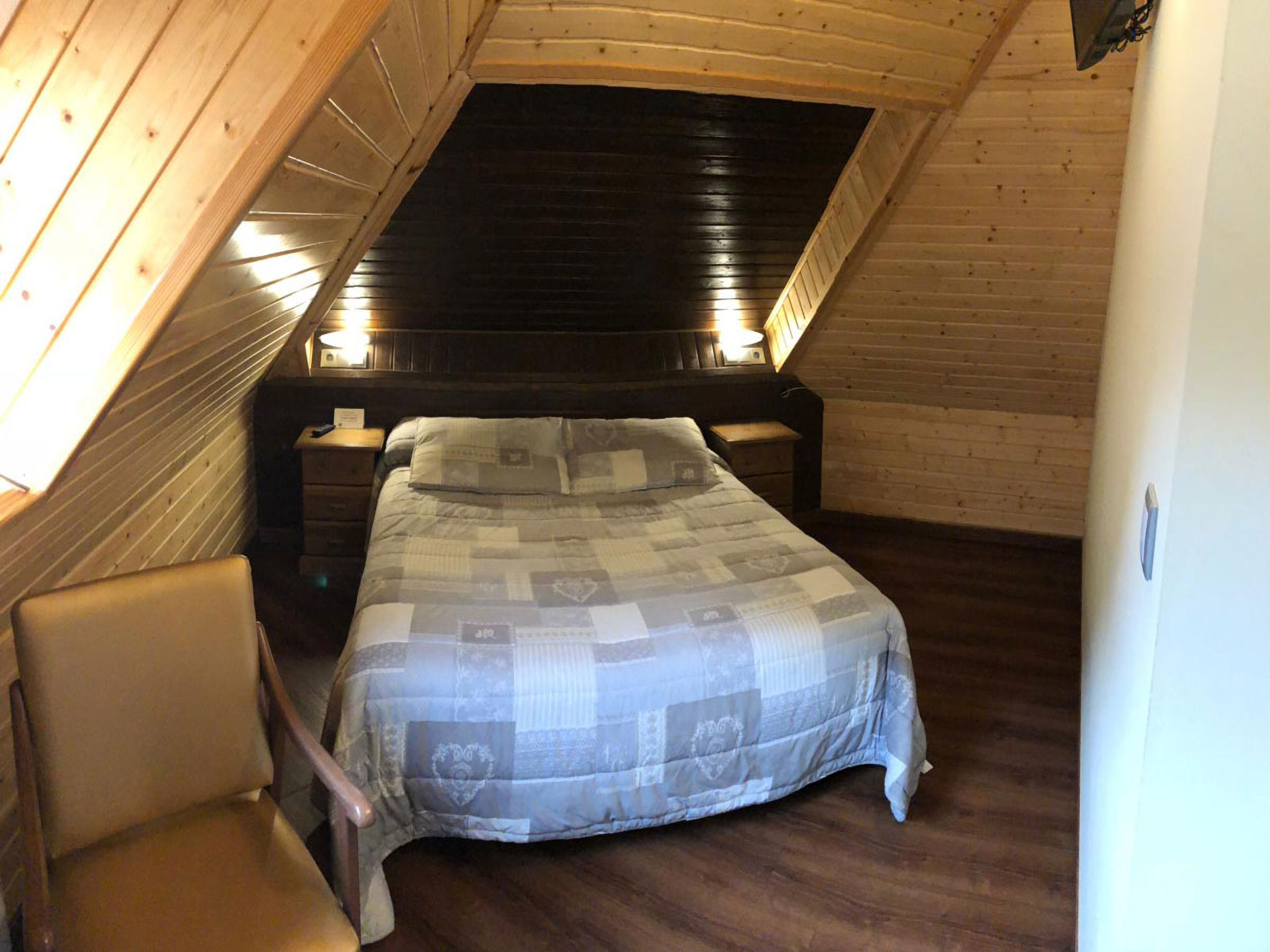 Ett sovrum med ett sluttande tak, en säng med ett mönstrat överkast, ett sängbord och en stol.
