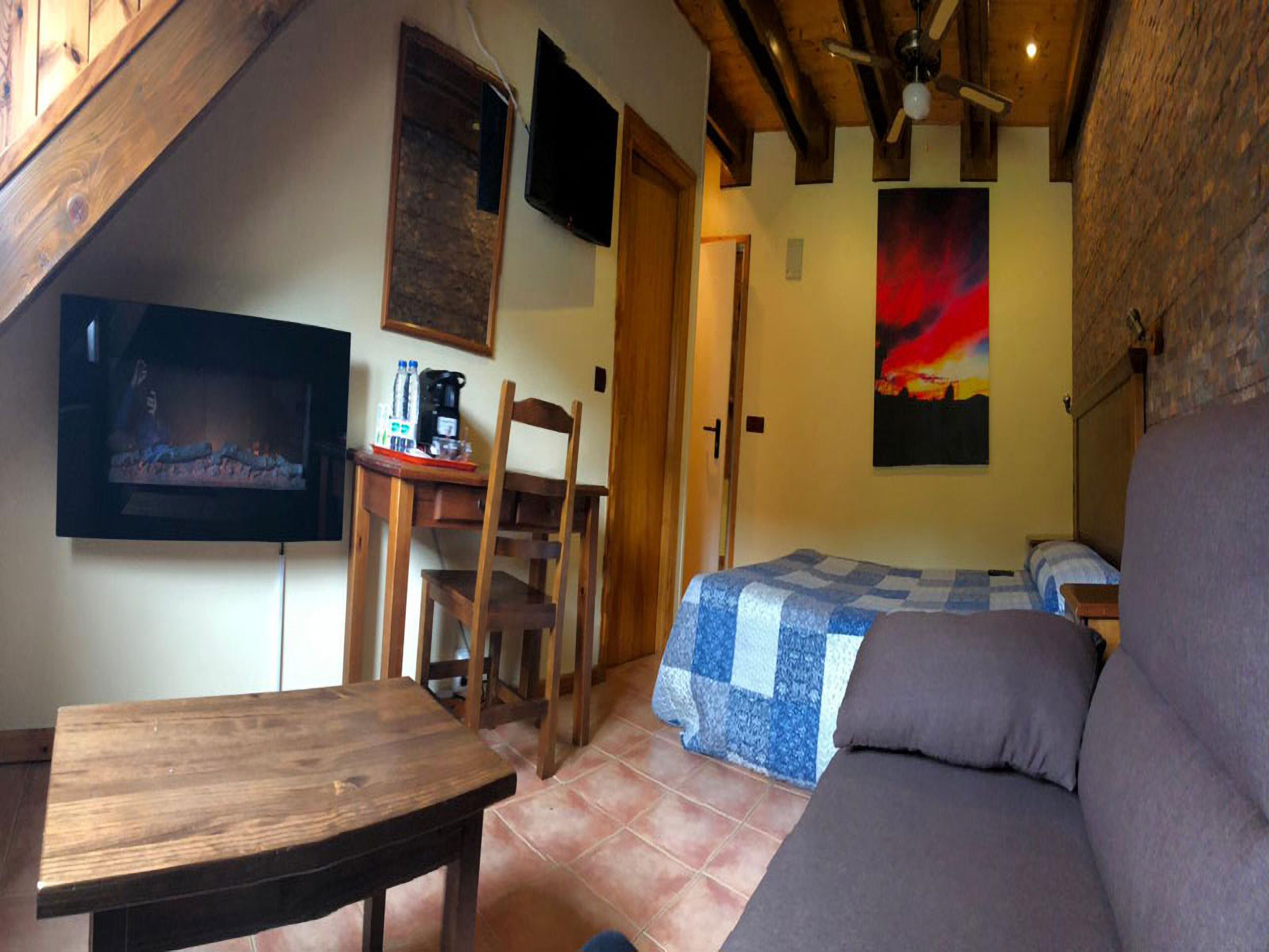 A cozy room with a wooden ceiling, a television, a bed with a blue and white quilt, a sofa, and a wooden table.