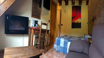 Una habitación acogedora con techo de madera, televisor, cama con colcha azul y blanca, sofá y mesa de madera.