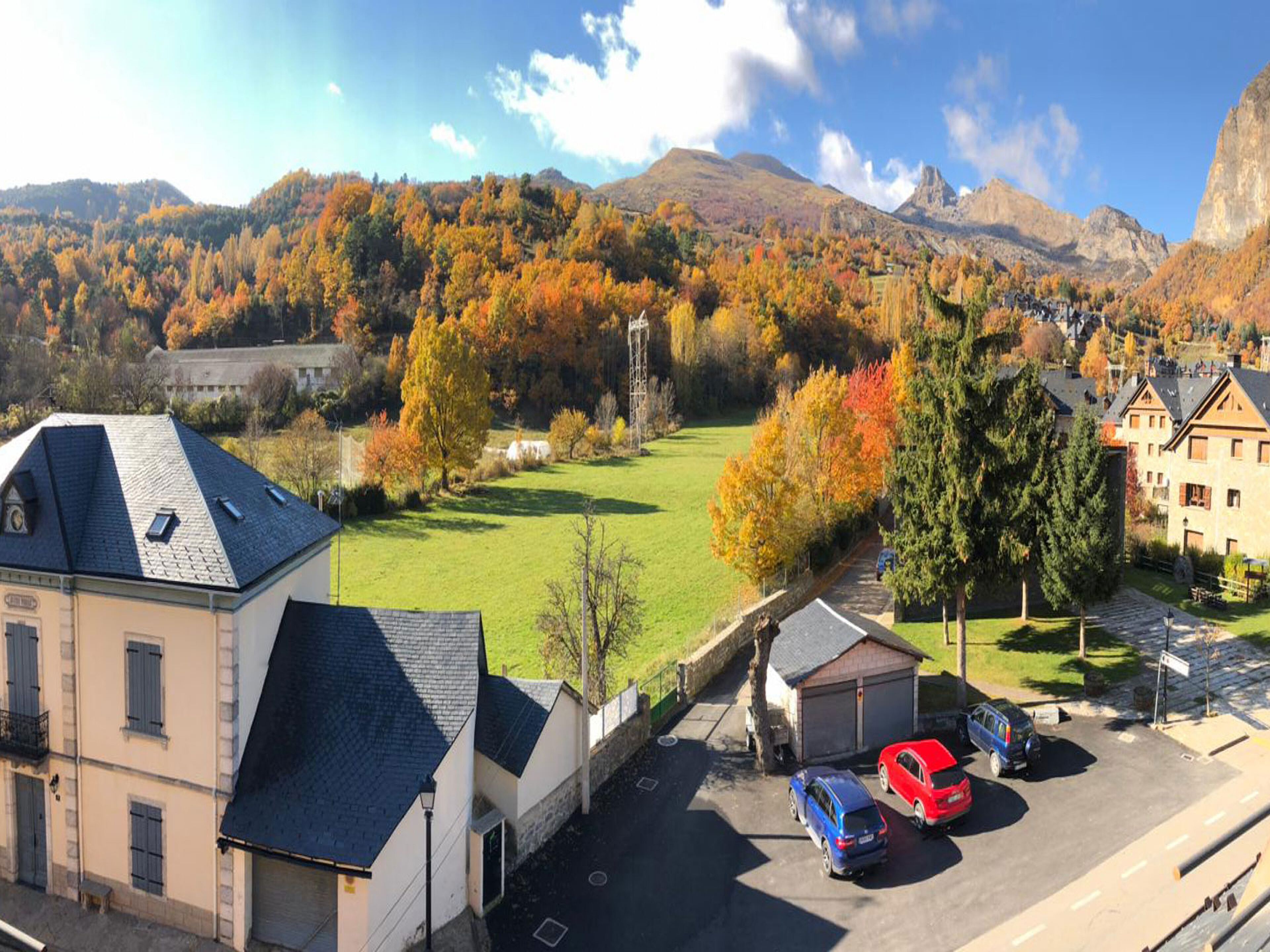 A hotel with a parking area, a grassy field, and a mountainous backdrop.