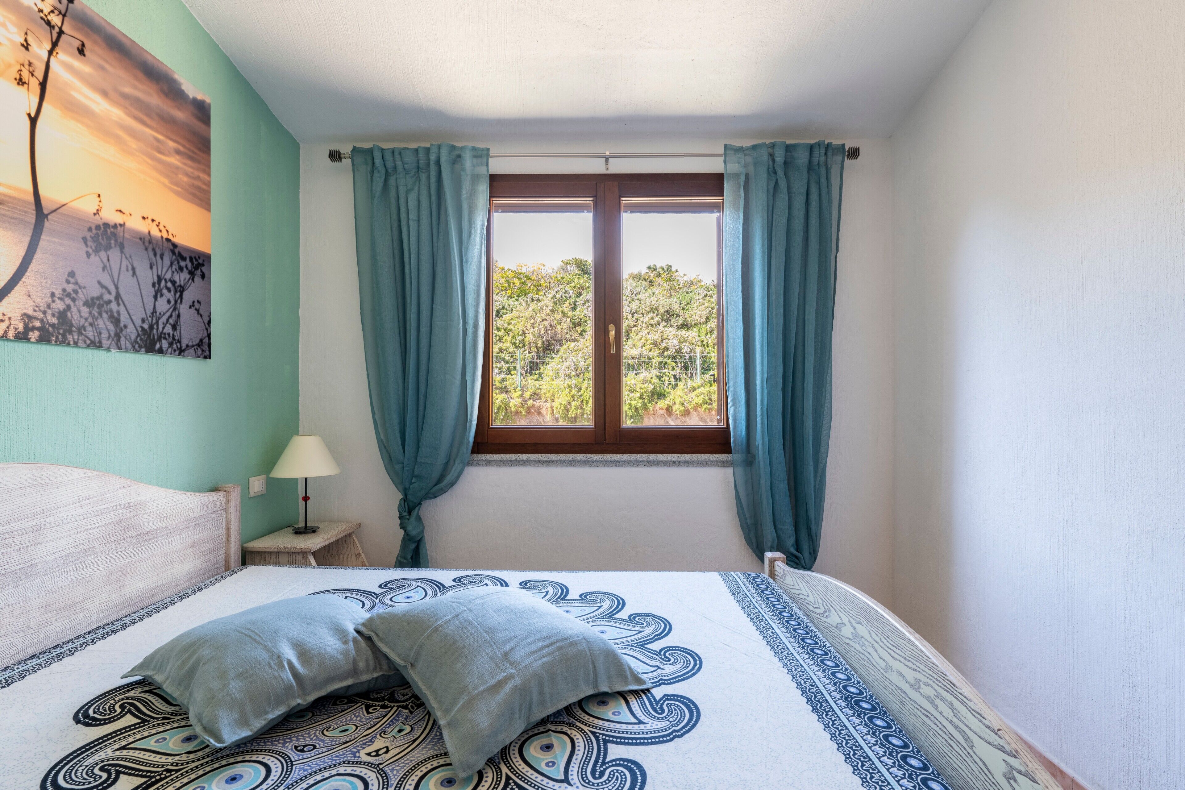 Ein Schlafzimmer mit Bett, Vorhängen, einem Fenster und einem Wandbild.