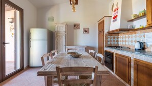 A kitchen with a dining table, chairs, a refrigerator, cabinets, and a tiled backsplash. - Villa 'Casa Joy' with Sea View, Wi-Fi and Air Conditioning (Tertenia)