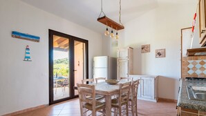A kitchen with a dining table, chairs, a refrigerator, and a hanging light fixture. - Villa 'Casa Joy' with Sea View, Wi-Fi and Air Conditioning (Tertenia)