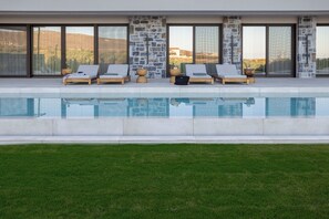 A modern poolside area with lounge chairs, a stone wall, and a clear view of the landscape. - Olea Hill Villas - Villa Cave by Estia (Hersonissos)