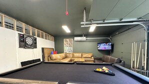 Une salle de billard équipée d’une table de billard, de canapés en cuir, d’un jeu de fléchettes et d’un téléviseur.