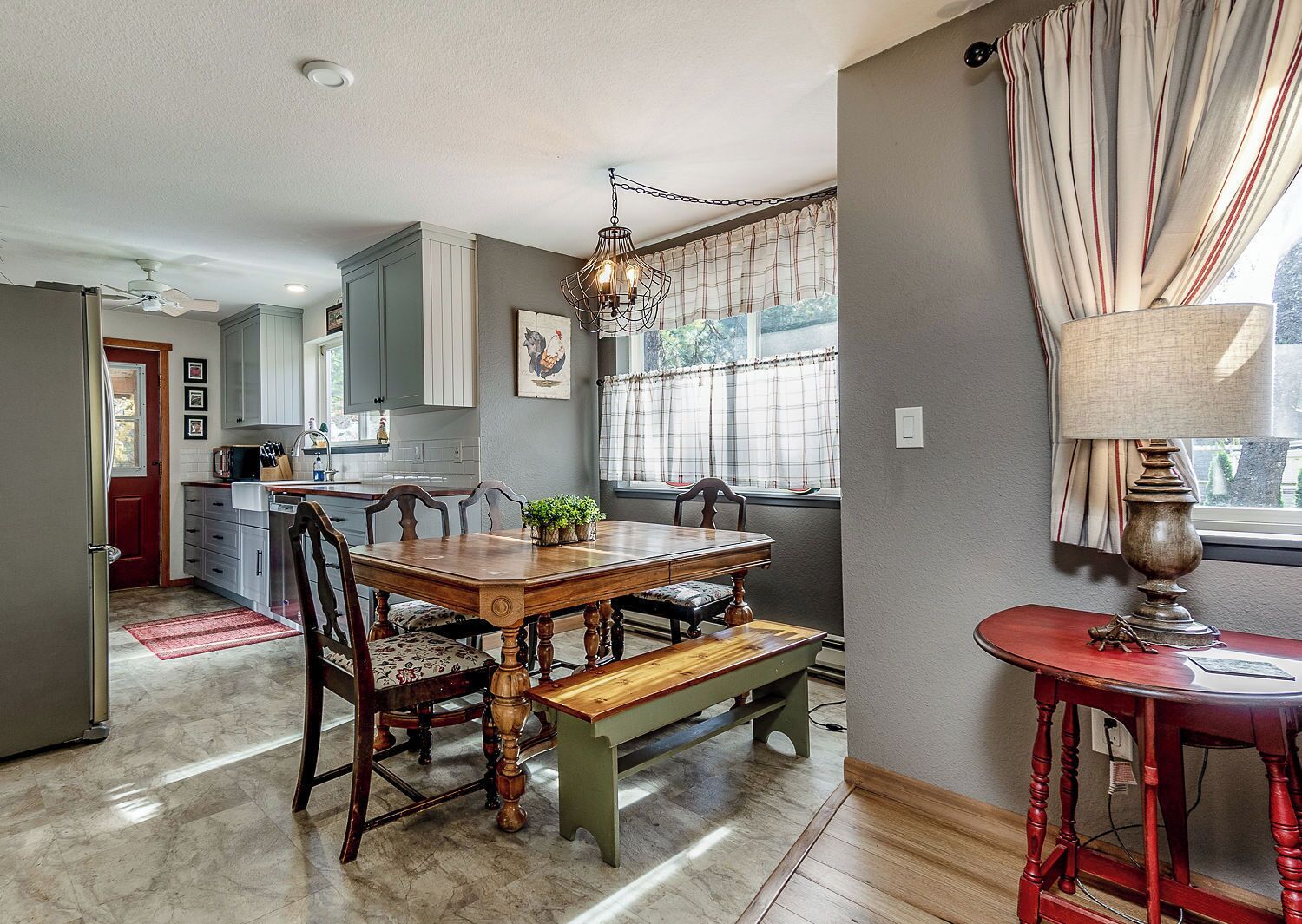A dining area with a wooden table, chairs, a chandelier, and a window with curtains.