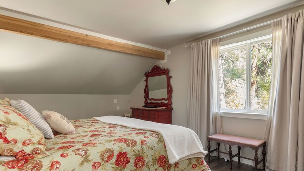 Une chambre à coucher avec un lit, un banc en bois, un miroir et une fenêtre avec des rideaux.