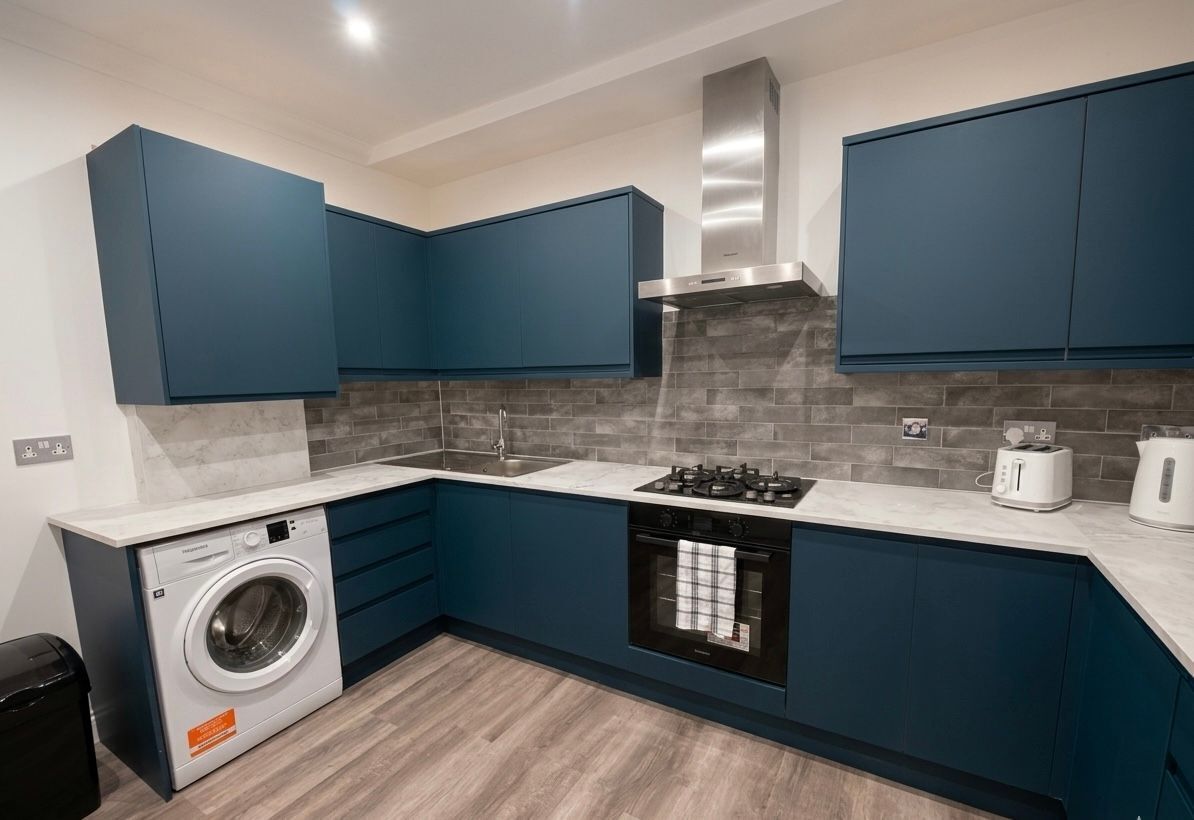 A modern kitchen with blue cabinets, a built-in washing machine, a stove, and a toaster.