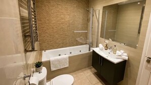 A modern bathroom with a bathtub, toilet, sink, and a large mirror. - Boswell Elite Two Bed Apartment (Croydon)