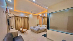 A hotel room with a bed, a desk, a chair, a TV, and a large window. - Avron Beach Resort (Daman)
