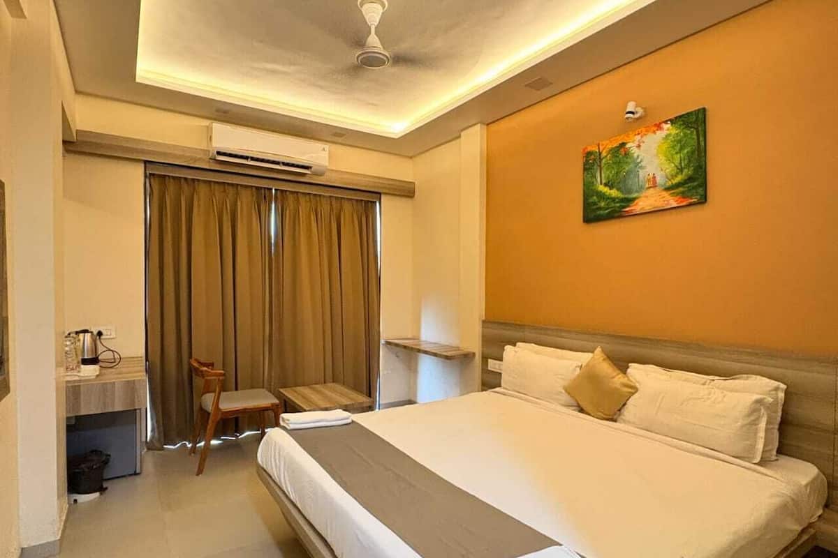 A hotel room with a large bed, a desk with a chair, an air conditioning unit, and a painting on the wall.