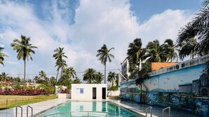 A swimming pool with a mural on the adjacent wall, surrounded by palm trees and a clear sky. - Avron Beach Resort (Daman)
