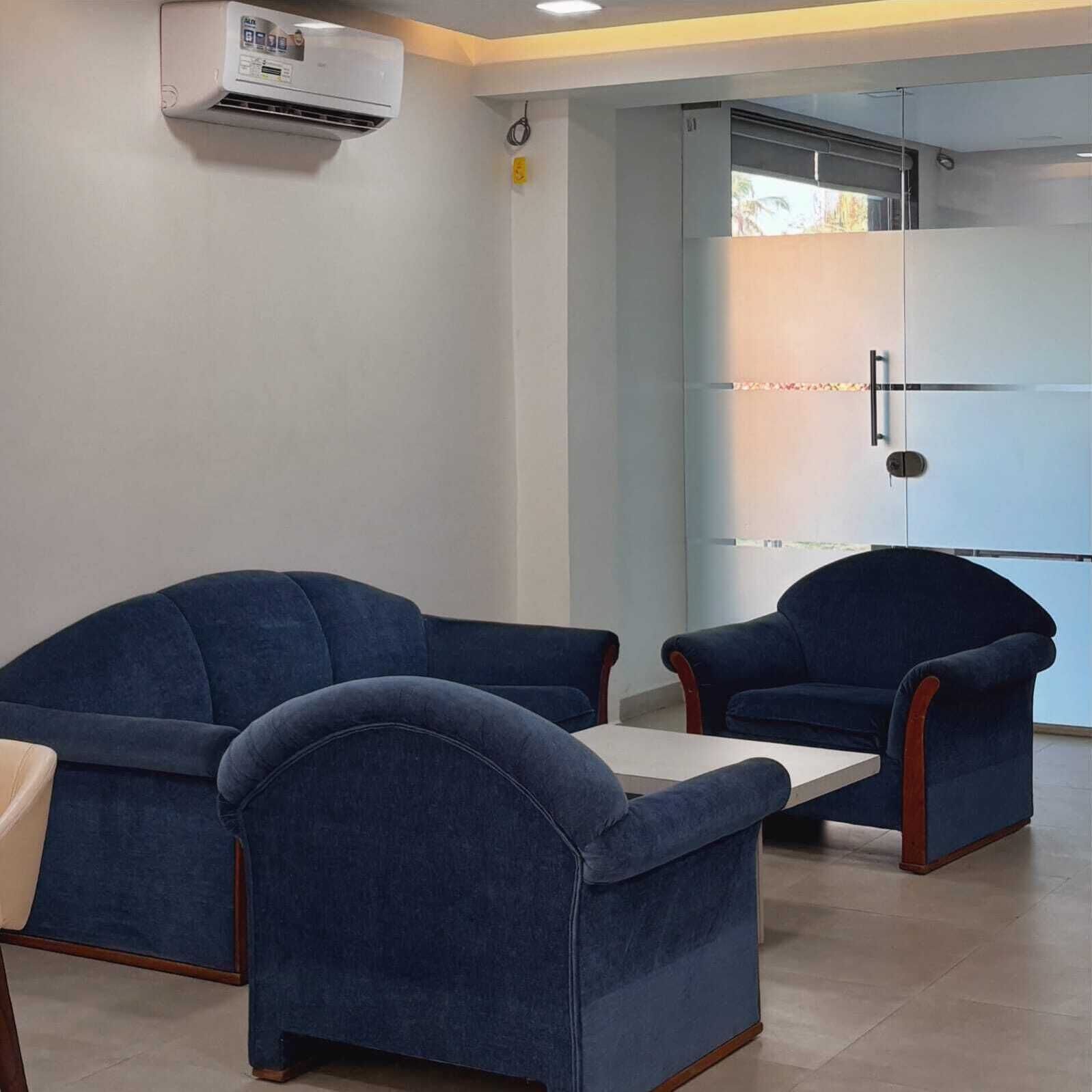 Un área de espera con dos sillones azules y una mesita. Un equipo de aire acondicionado está montado en la pared.