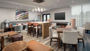A modern hotel lobby with a bar area, seating arrangements, a fireplace, and a large TV mounted on the wall. - Near Logan Airport + Free Breakfast. Shuttle. Gym. (Chelsea)
