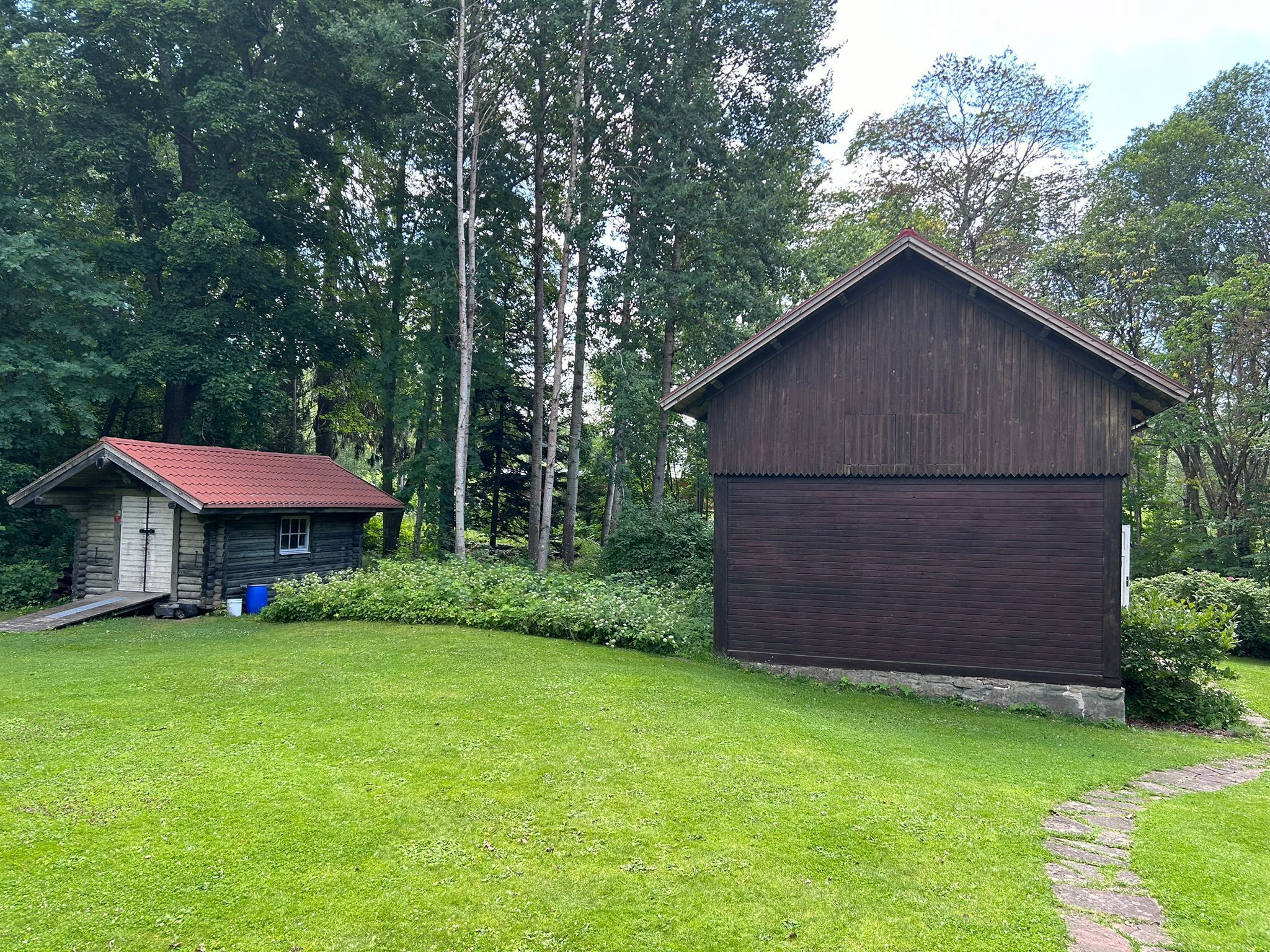A rustic cabin with a red roof and a larger wooden structure with a closed shutter.