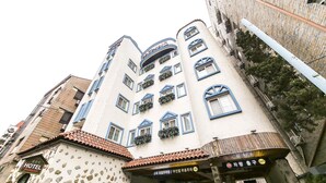 Un edificio de varios pisos con un diseño arquitectónico único, con balcones adornados con plantas, fachada de piedra y un letrero que indica un hotel.