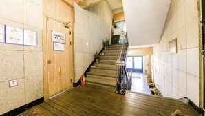 Una escalera de madera con barandilla, un cartel en la pared y una puerta con manija.