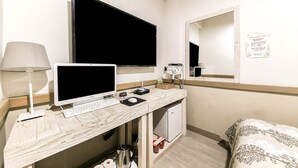 Habitación de hotel con escritorio, computadora, lámpara, secador de pelo y una cama.