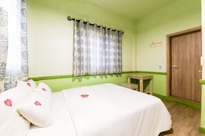 Una habitación con una cama, una mesita pequeña, una puerta de madera y una ventana con cortinas estampadas.