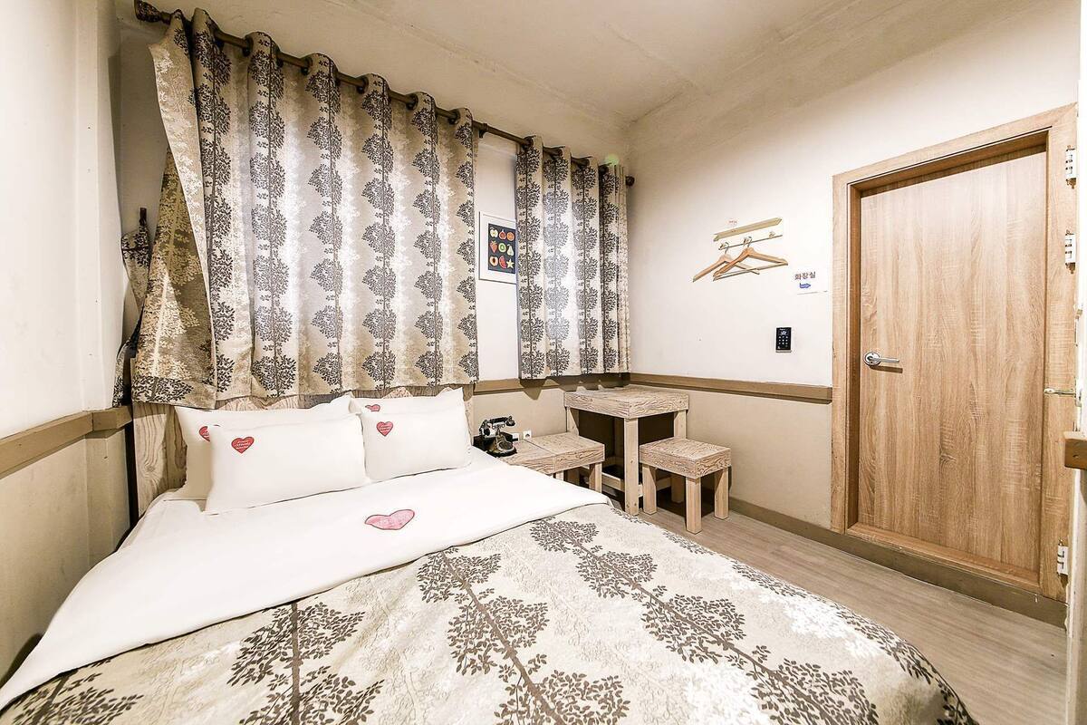 Une chambre à coucher comprenant un lit, un bureau, une chaise, une armoire et un rideau orné d’un motif de feuilles.