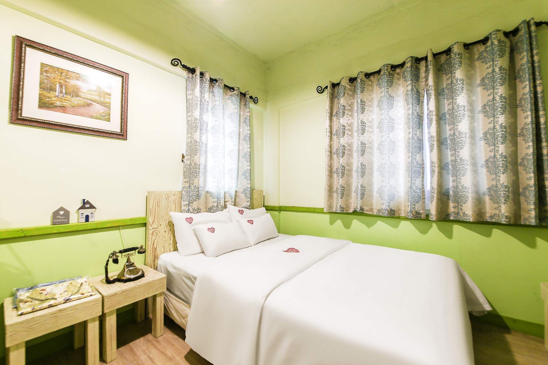 A room with a bed, a nightstand, a telephone, a framed picture, and patterned curtains.