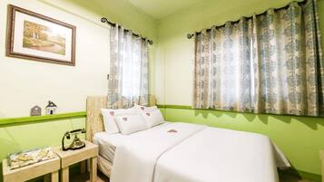 A room with a bed, a nightstand, a telephone, a framed picture, and patterned curtains.