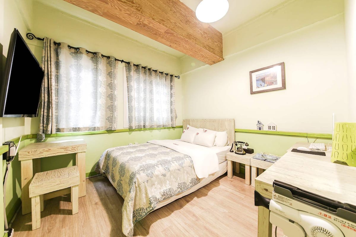 Une pièce comprenant un lit, un bureau, une chaise, une petite table, un téléphone, un tableau accroché au mur et un luminaire au plafond.
