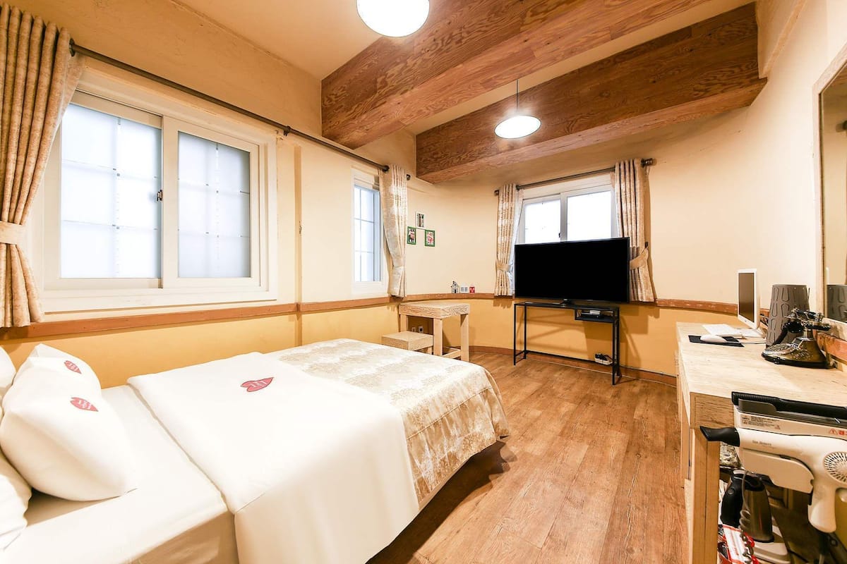 Une chambre d’hôtel avec un lit, un bureau avec un ordinateur, une télévision et une fenêtre.