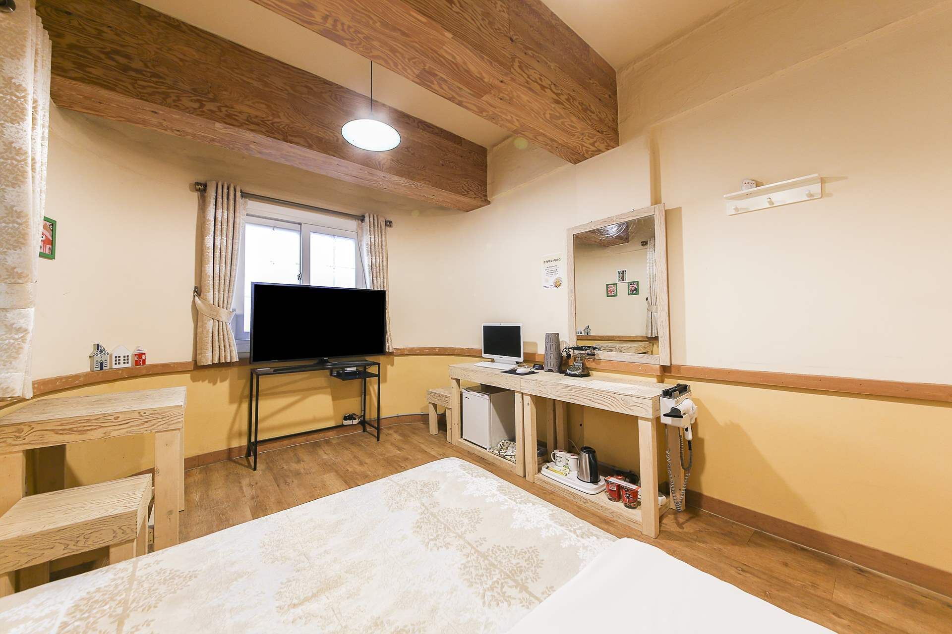 Habitación de hotel con techo de madera, un televisor, un escritorio con ordenador, un espejo y una cama.
