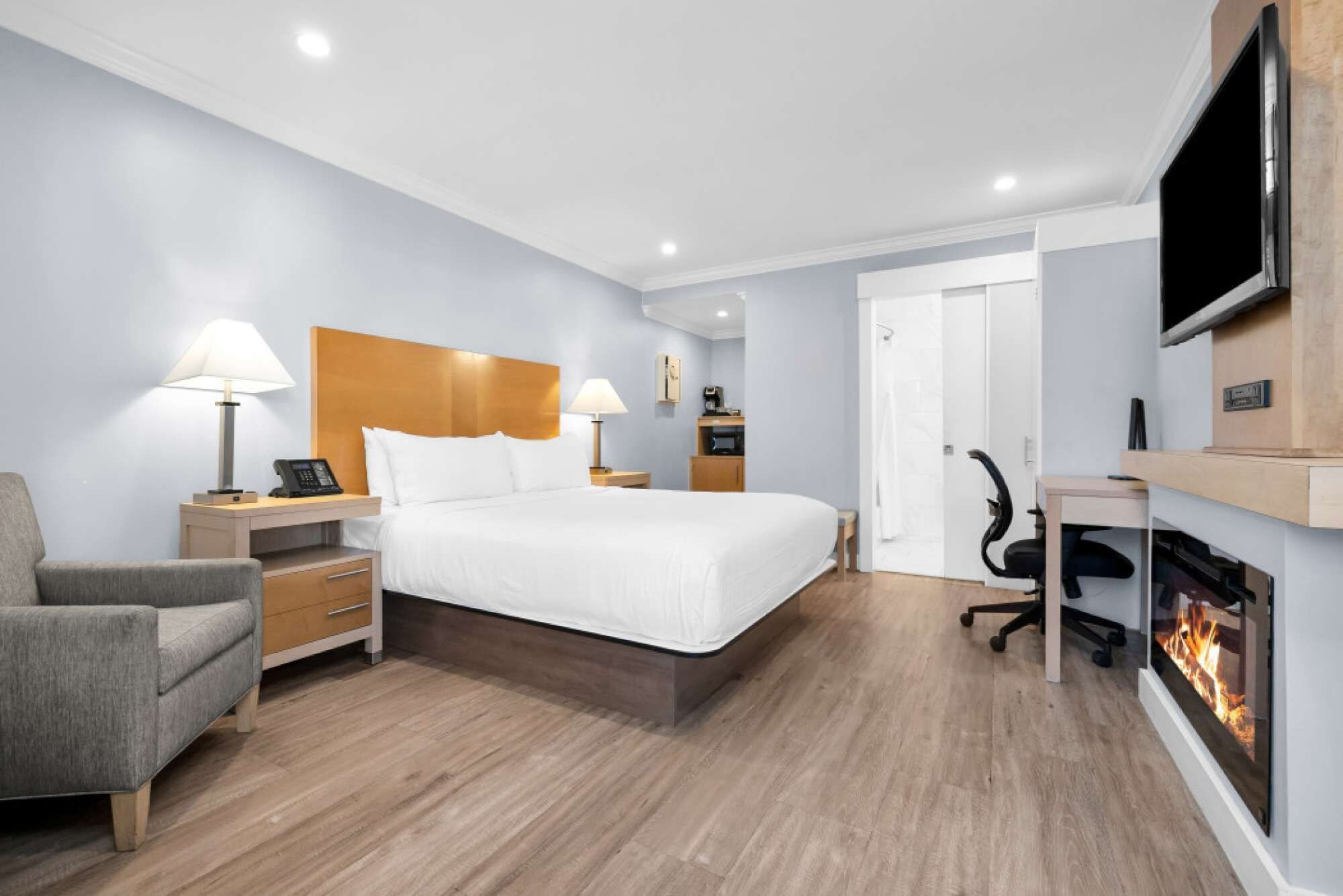 A hotel room with a bed, bedside tables, a chair, a desk, a television, and a fireplace.