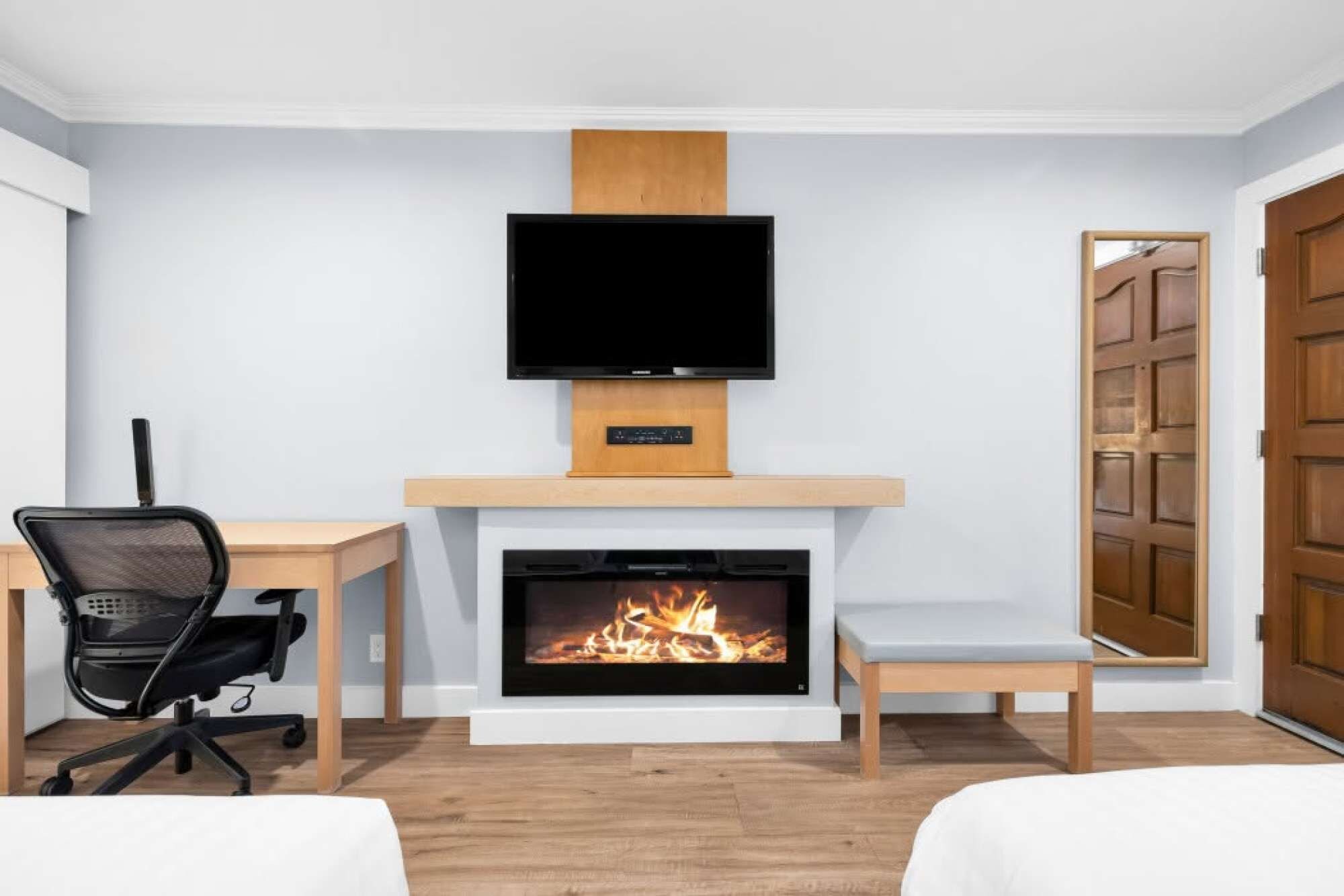 A modern room with a fireplace, a television mounted above it, a desk with a chair, and a bed.