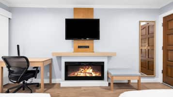 A modern room with a fireplace, a television mounted above it, a desk with a chair, and a bed.