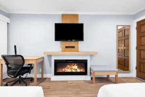 Een moderne kamer met een open haard, een televisie erboven, een bureau met stoel en een bed.