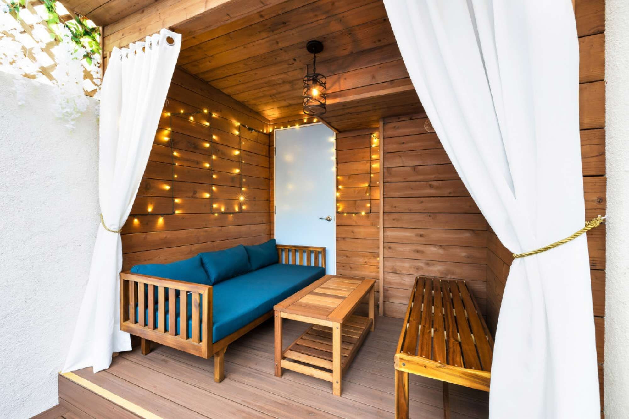 A cozy wooden deck with a blue sofa, a small table, and string lights.