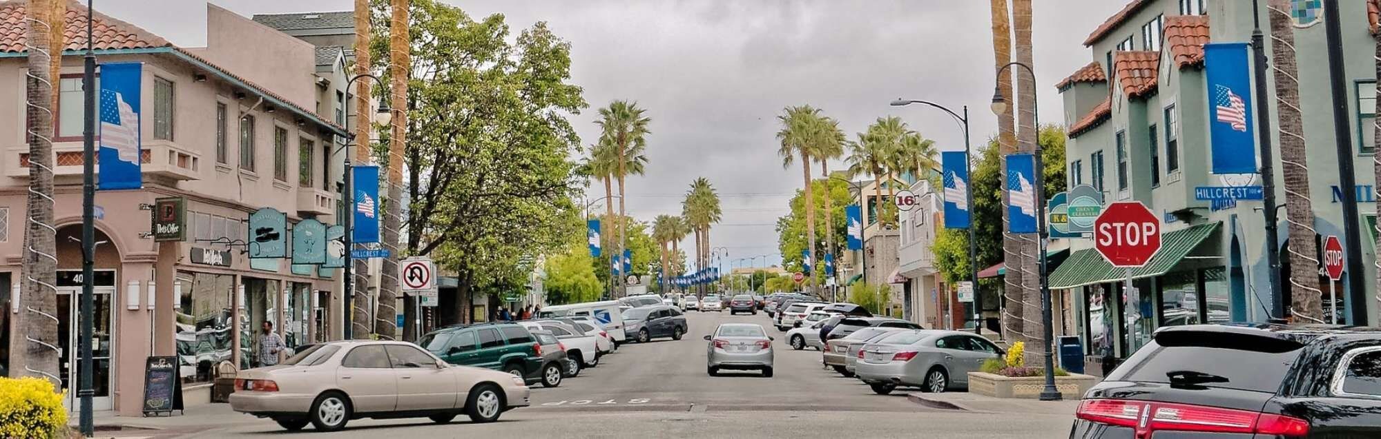 A street lined with parked cars and buildings, including a stop sign and a no parking sign.