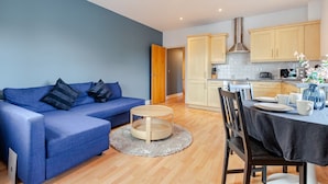 Una sala de estar moderna con un sofá azul, una mesa de centro redonda y un comedor con una mesa dispuesta para dos personas.