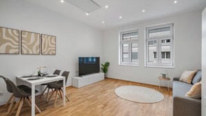Een moderne woonkamer met een eethoek, een flatscreen televisie en een grijze bank.