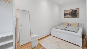 Een moderne slaapkamer met een wit bed, een klein nachtkastje, een witte kledingkast en een schilderij aan de muur.