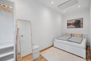 Ein modernes Schlafzimmer mit einem weißen Bett, einem kleinen Nachttisch, einem weißen Kleiderschrank und einem Gemälde an der Wand.