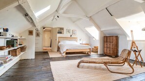 A loft bedroom with a sloped ceiling, a wooden bed, a wicker chair, and a wooden cabinet. - Stunning 8-Bedroom Home in Painswick (Painswick)