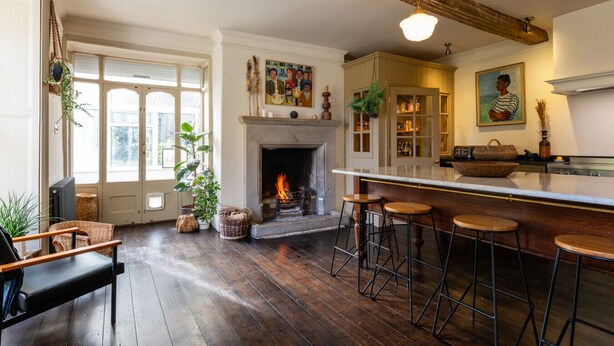 A cozy kitchen with a fireplace, wooden bar stools, and a dining area with a chair. - Stunning 8-Bedroom Home in Painswick (Painswick)