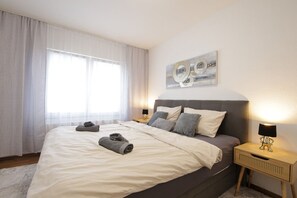 A neatly made bed with pillows and rolled towels, a bedside lamp, and a painting on the wall.