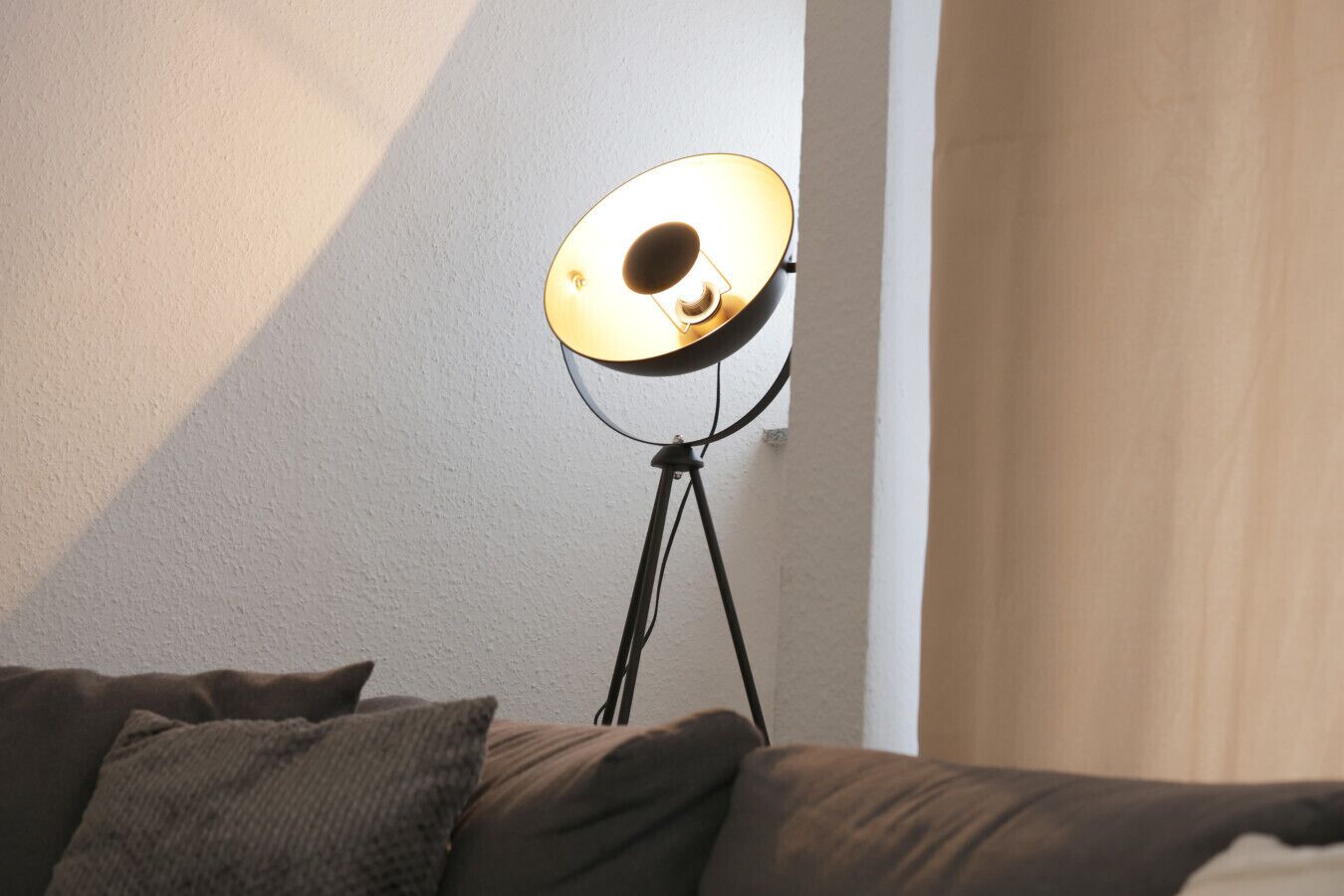 A lamp on a tripod stand in a room with a bed and a wall.