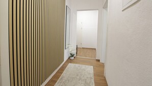 A hallway with a wooden floor, a white rug, a potted plant, and a door at the end. - StayBaran XL - 6 Betten I 3 Schlafzimmer I Parkplatz I (Essen)