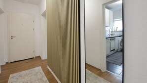 A hallway with a white door, a vertical wooden panel, and a view into a kitchen with a washing machine. - StayBaran XL - 6 Betten I 3 Schlafzimmer I Parkplatz I (Essen)