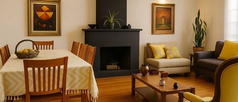 A dining area with a table set for four, a fireplace, and a living room with a sofa and armchairs.