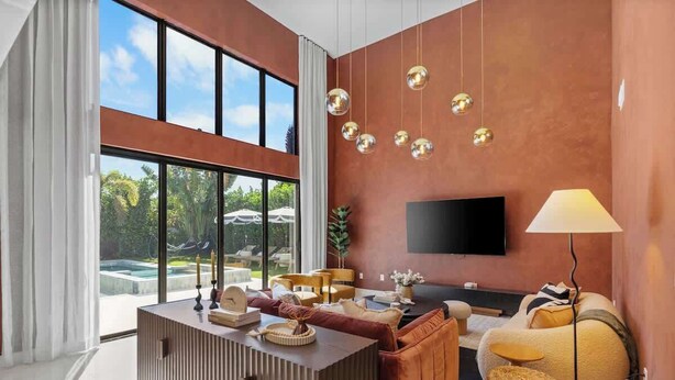 Una sala de estar moderna con un ventanal grande, un televisor de pantalla plana, un sofá, una mesa de centro y una lámpara.
