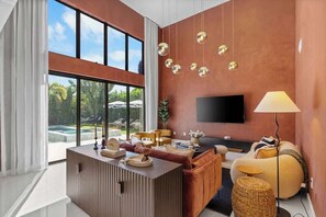 Un salon moderne doté d’une grande fenêtre, d’un téléviseur à écran plat, d’un canapé, d’une table basse et d’une lampe.