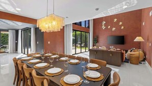 Un comedor moderno con una mesa grande dispuesta para una comida, una araña y un televisor en la pared.
